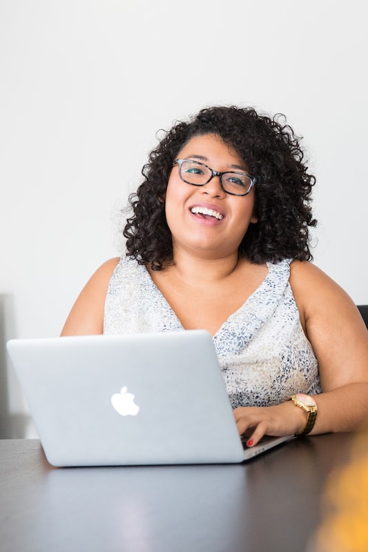 Frau mit Brille sitzt lächelnd an am Laptop